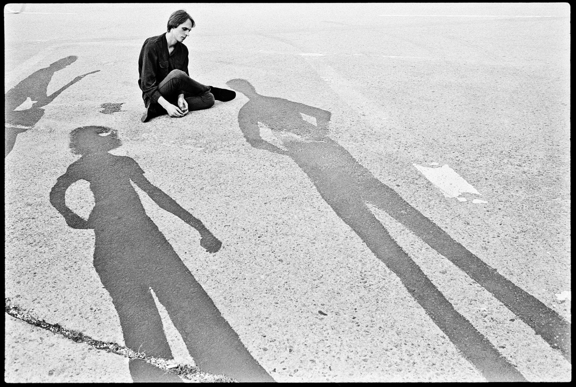 Person sitting on pavement with long shadows